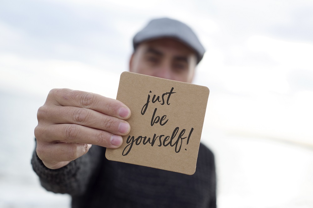 man shows signboard with the text just be yourself